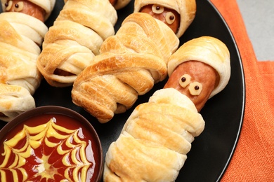 Spooky sausage mummies and sauce for Halloween party on plate, closeup