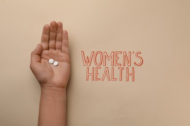 Photo of Girl holding pills near text Women's Health on beige background, top view