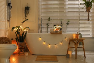 Stylish bathroom interior with green houseplants and string lights. Idea for design