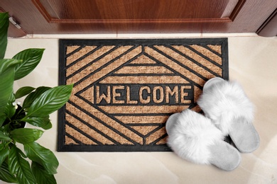 Welcome doormat and white slippers at door in hall, top view