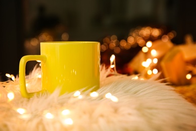 Yellow cup with hot drink and fairy lights on faux fur