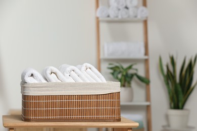 Wicker basket with folded soft terry towels on wooden table indoors, space for text