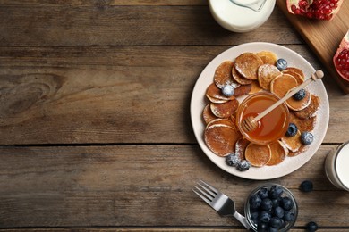 Delicious mini pancakes cereal with blueberries and honey served on wooden table, flat lay. Space for text