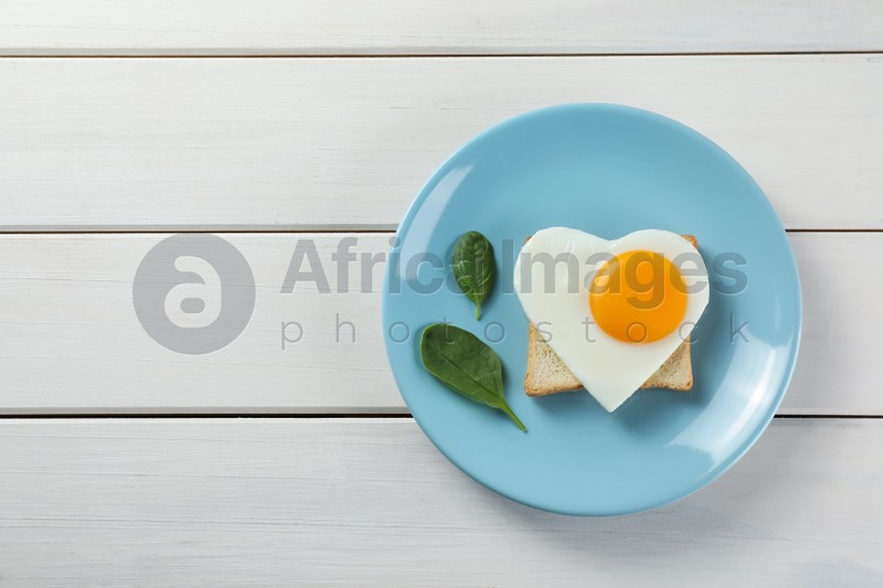 Romantic breakfast with heart shaped fried egg, toast and spinach on white wooden table, top view. Space for text