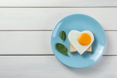 Photo of Romantic breakfast with heart shaped fried egg, toast and spinach on white wooden table, top view. Space for text