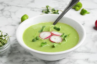 Bowl of broccoli cream soup with radish and microgreens served on white marble table