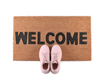 Stylish door mat with word Welcome and shoes on white background, top view