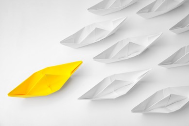 Photo of Group of paper boats following yellow one on white background, flat lay. Leadership concept