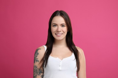 Beautiful woman with tattoos on arm against pink background