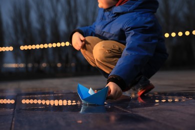 Little boy playing with paper boat near puddle outdoors, closeup