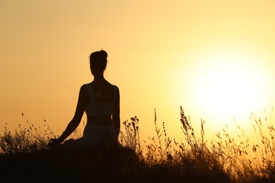 Photo of Silhouette of woman meditating outdoors at sunset, back view. Space for text