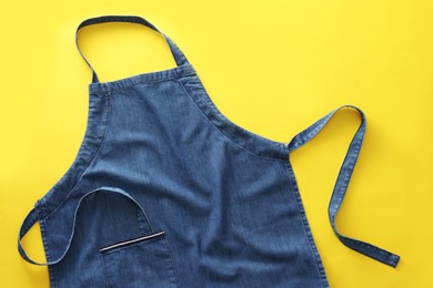 Denim blue kitchen apron on yellow background, top view