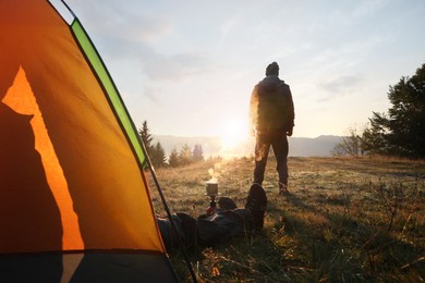 People near camping tent in mountains at sunset, back view