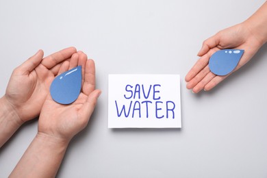 Photo of People holding paper drops near card Save Water on light grey background, top view