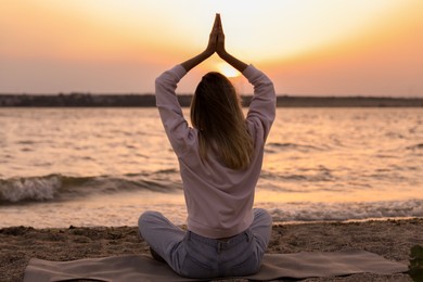 Young woman meditating on beach near river at sunset, back view
