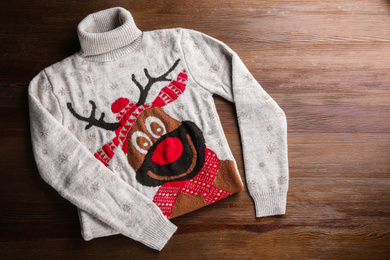Photo of Warm Christmas sweater with deer on wooden table, top view