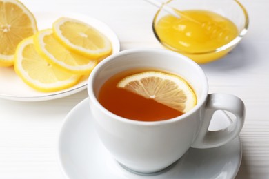 Cup with delicious immunity boosting tea, lemon and honey on white wooden table, closeup