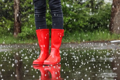 Woman wearing red rubber boots outdoors on rainy day with hail, closeup 