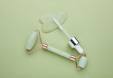 Jade gua sha tool, facial roller and dropper on light green background, flat lay