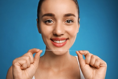 Young woman flossing her teeth on blue background. Cosmetic dentistry