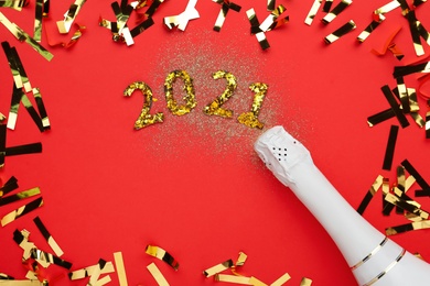 Flat lay composition with number 2021 made of shiny glitters near champagne bottle and confetti on red background
