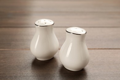 Photo of White ceramic salt and pepper shakers on wooden table, closeup