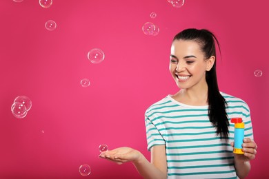 Young woman having fun with soap bubbles on pink background, space for text