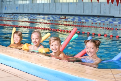 Little kids with swimming noodles in indoor pool