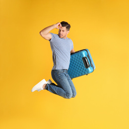 Handsome man with suitcase for summer trip jumping on yellow background. Vacation travel