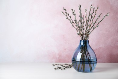 Beautiful bouquet of pussy willow branches in vase on white wooden table. Space for text