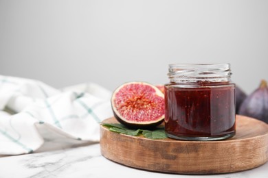 Photo of Glass jar of tasty sweet fig jam and fruits on white marble table. Space for text