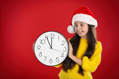 Photo of Girl in Santa hat with clock on red background. New Year countdown