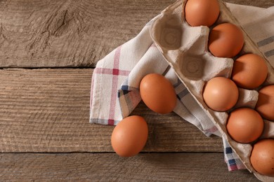 Photo of Raw chicken eggs in carton and napkin on wooden table, flat lay. Space for text