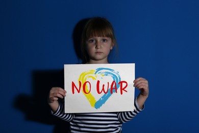 Sad little girl holding paper with phrase No War on blue background