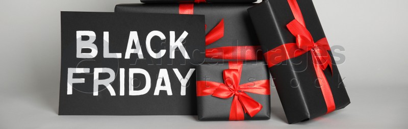 Many gift boxes and sheet of paper with words Black Friday on light grey background. Banner design