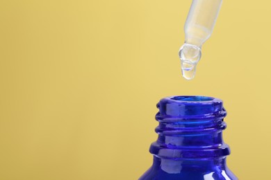 Photo of Dripping serum from pipette into bottle on yellow background, closeup. Space for text