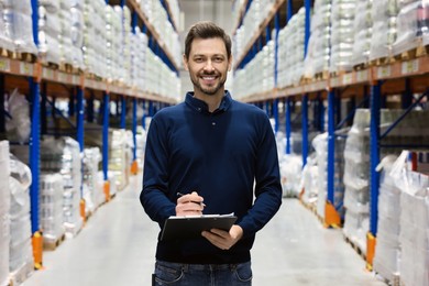 Happy manager holding clipboard in warehouse with lots of products