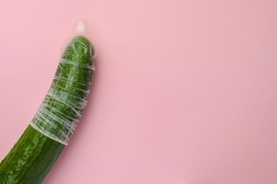 Cucumber with condom on pink background, top view and space for text. Safe sex concept