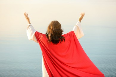 Jesus Christ raising hands near water outdoors, back view