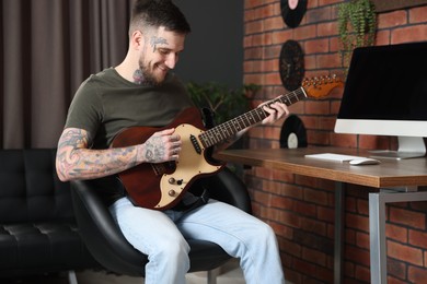 Photo of Smiling hipster man playing guitar in stylish room