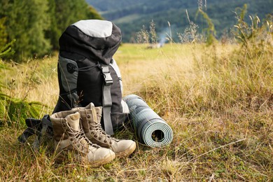 Photo of Backpack, boots and sleeping mat on hill, space for text. Tourism equipment