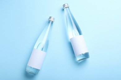 Glass bottles of water with blank label on light blue background, flat lay