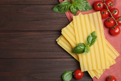 Uncooked lasagna sheets with cherry tomatoes and basil on wooden table, flat lay. Space for text