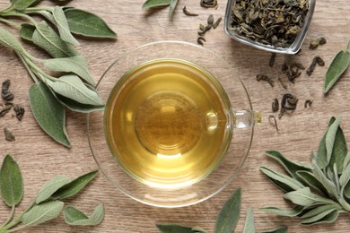 Cup of aromatic sage tea, dry and fresh leaves on wooden table, flat lay