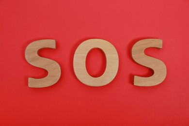 Abbreviation SOS made of wooden letters on red background, top view