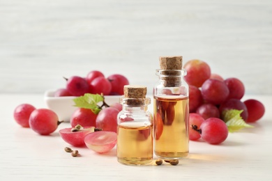 Organic red grapes, seeds and bottles of natural essential oil on white wooden table