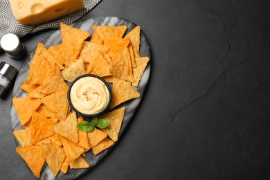 Photo of Delicious nachos and cheese sauce with basil on black table, flat lay. Space for text