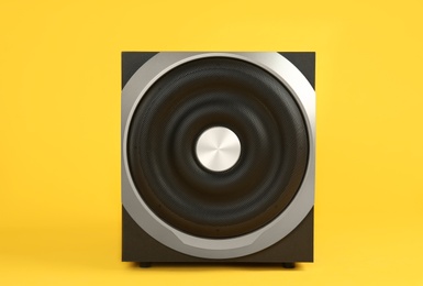 Modern subwoofer on yellow background. Powerful audio speaker