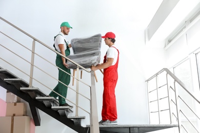 Male movers carrying armchair in new house
