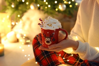Photo of Woman with cup of hot drink near Christmas tree indoors, closeup